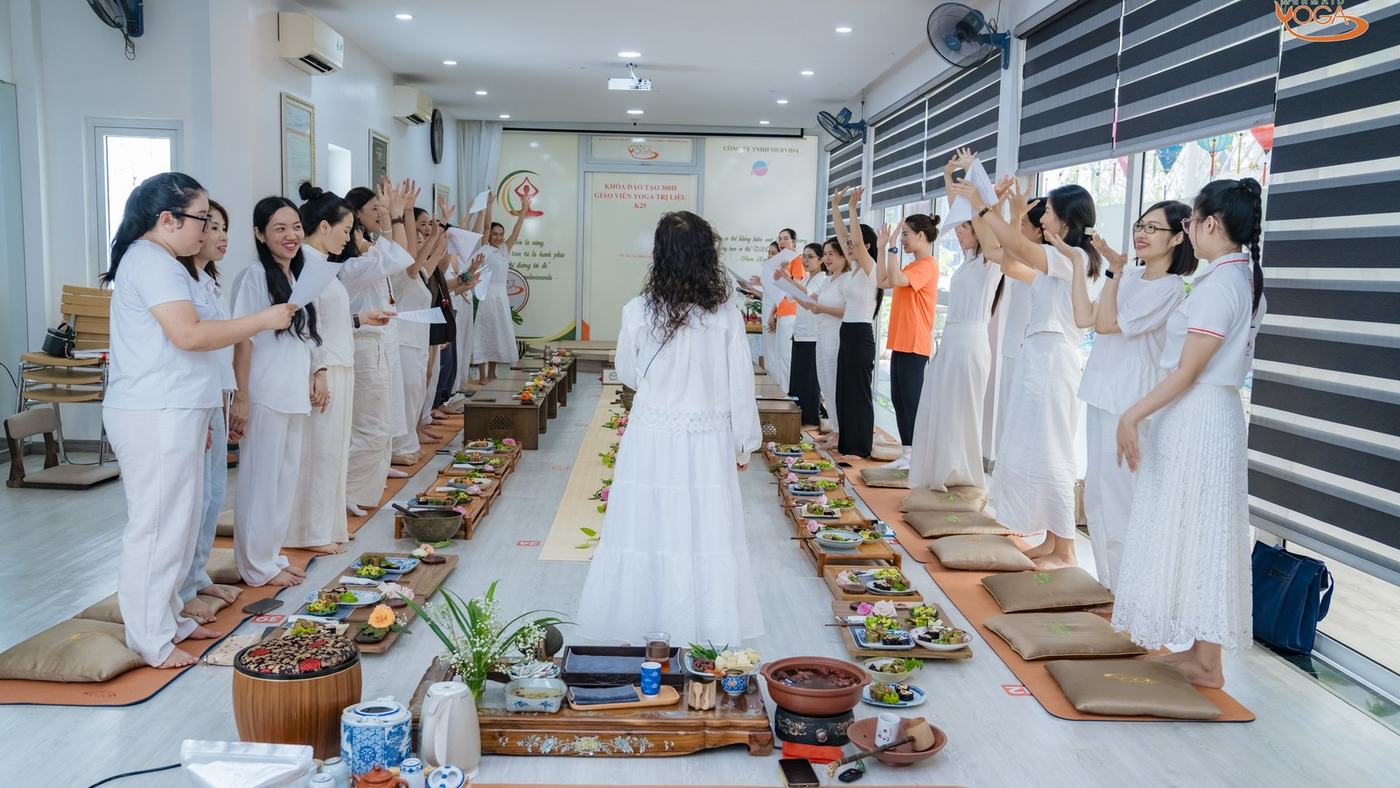 Cả lớp đứng hai bên bàn, mặt cười, giảng viên quay lưng ở giữa