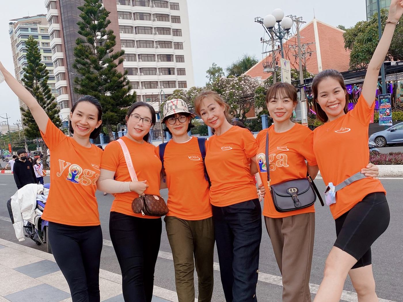 Nền gọn — nhóm sáu người đứng chỗ trống, sau lưng chỉ có trời và một toà nhà xa
